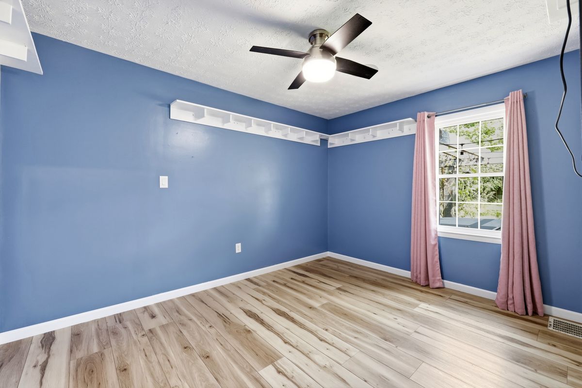 Bedroom with blue walls, ceiling fan, built-in shelf rail, and pink curtains