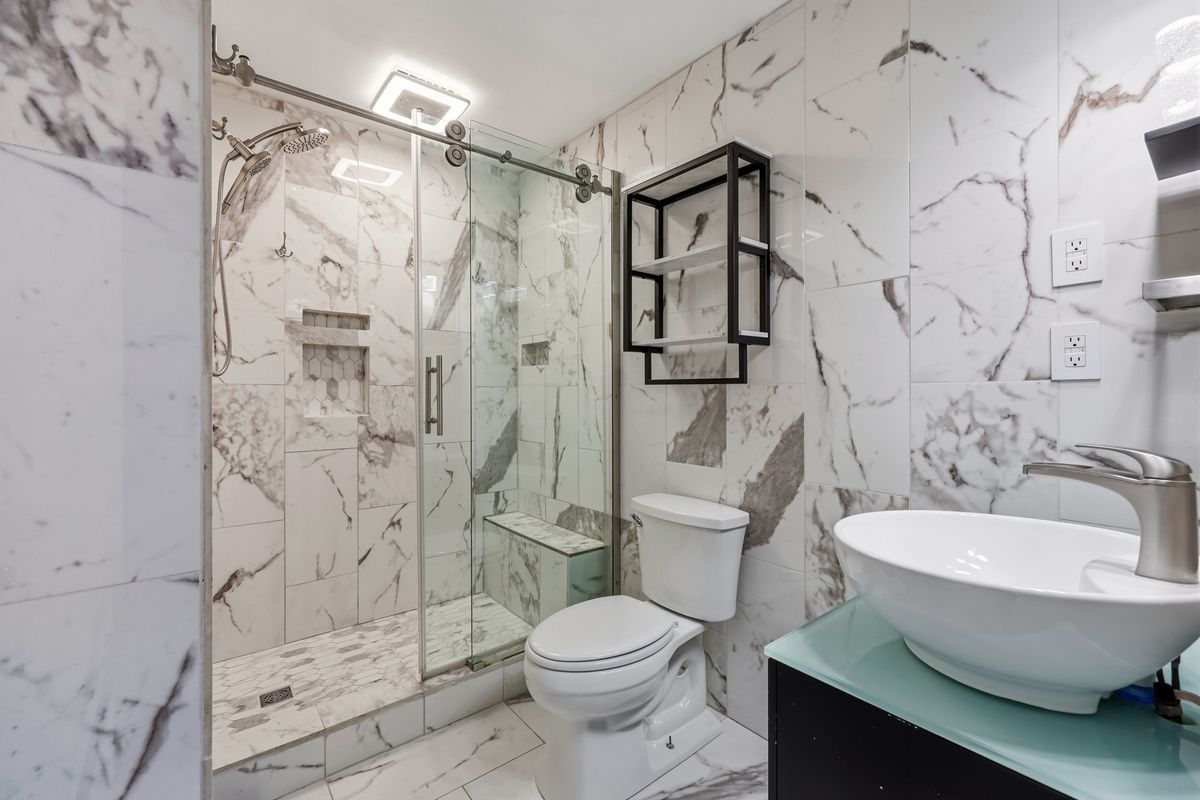 Marble-tiled bathroom with glass barn door shower, bench seat, and vessel sink