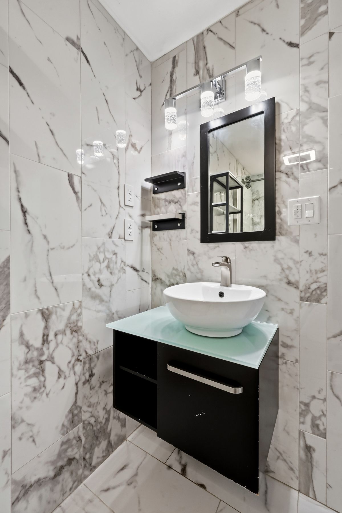 Floating vanity with vessel sink, glass top, and modern light fixture