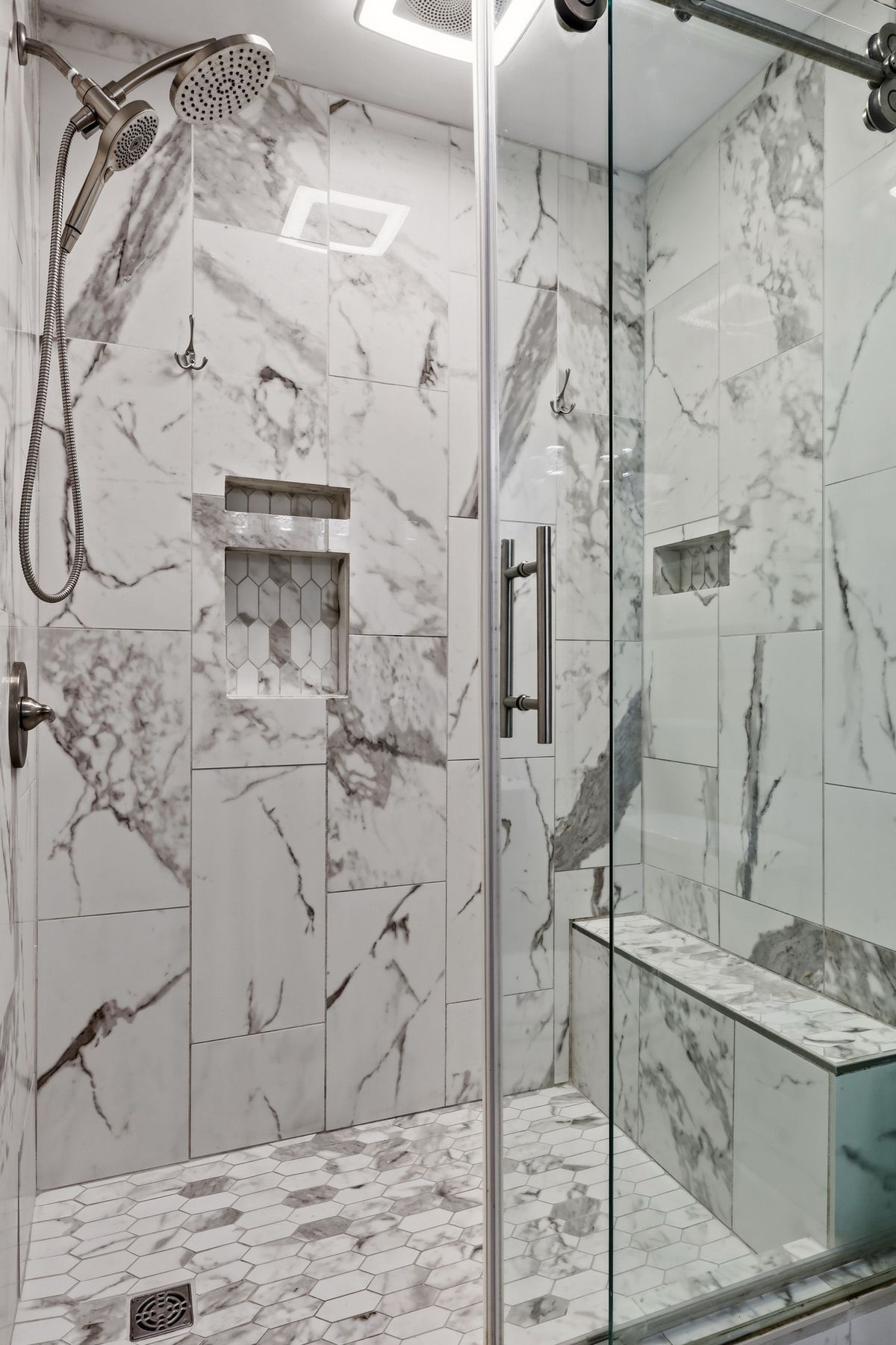 Shower detail with marble tile, built-in niche, bench seat, and hand shower