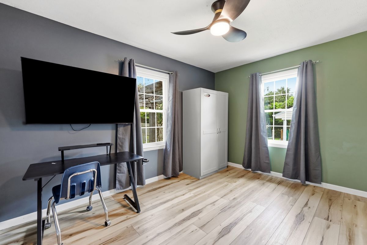 Bedroom or office with gray and green walls, desk, TV mount, and wardrobe