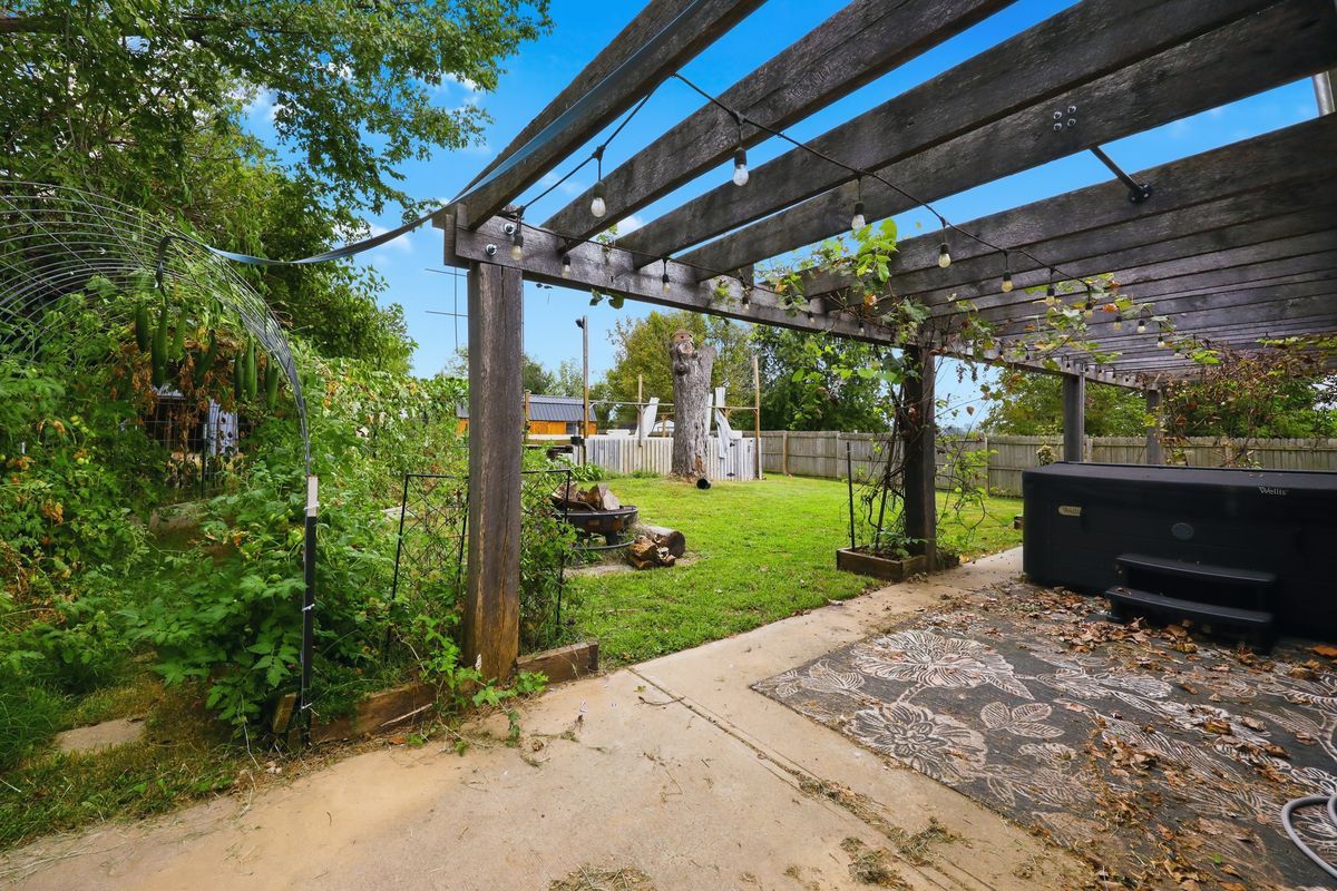 Pergola with string lights and grapevines beside garden area