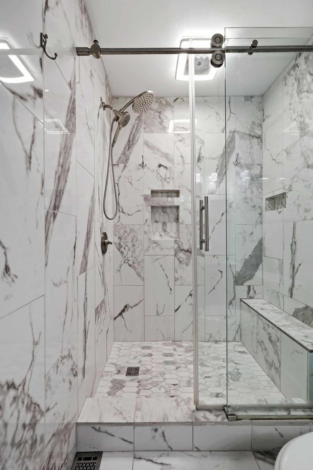Walk-in shower with marble tile, hexagon floor, barn door track, and niche