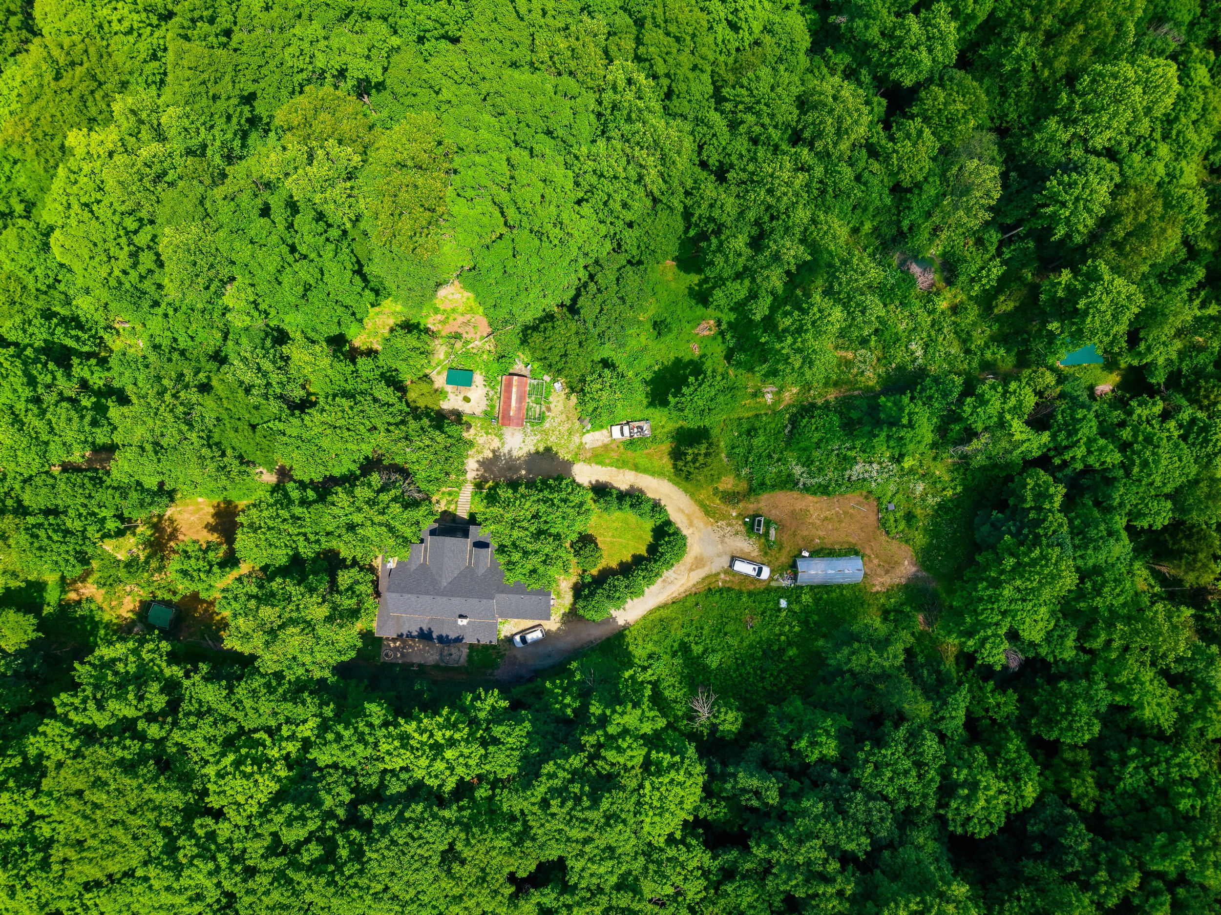 Aerial view of home, outbuildings, and wooded acreage