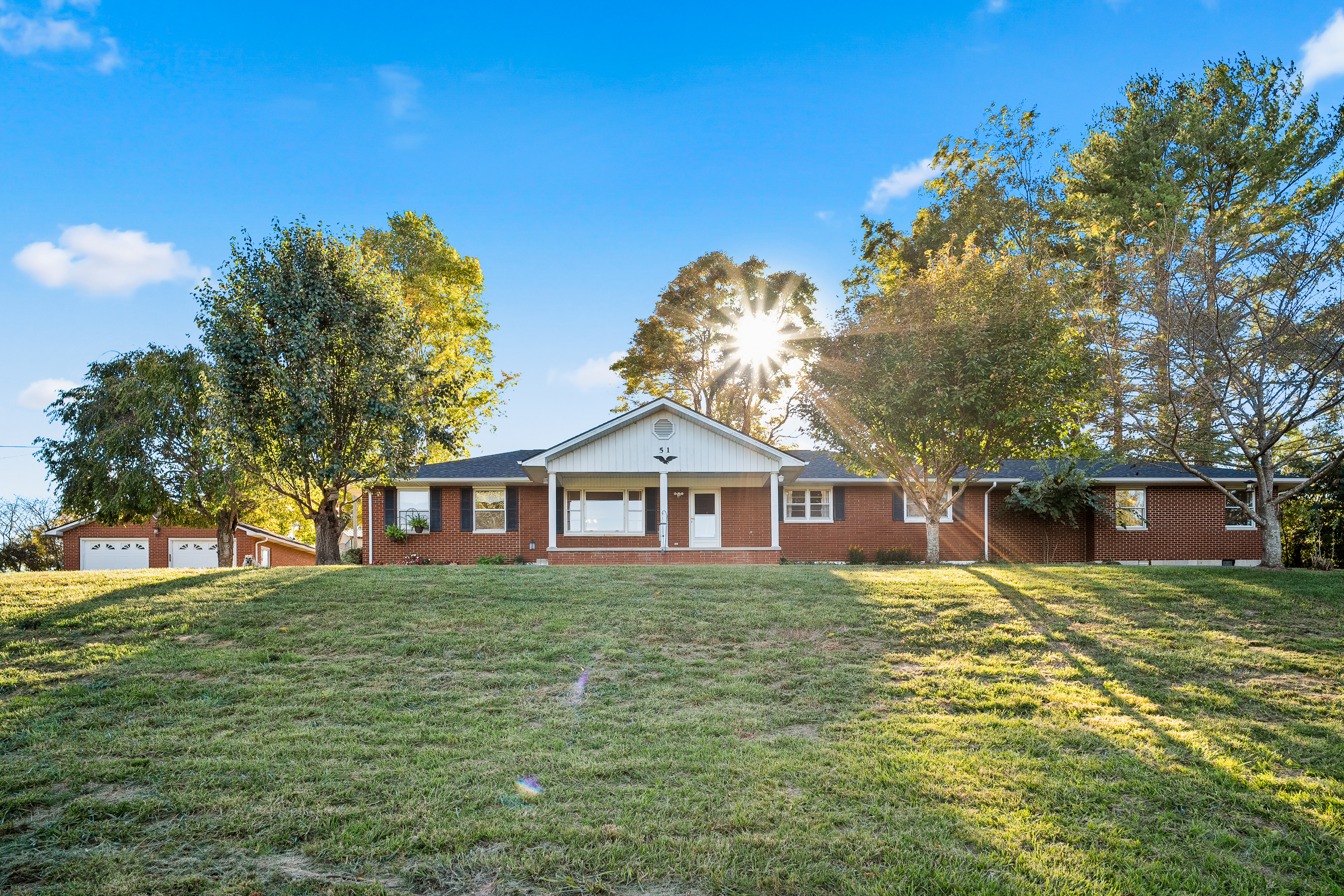 Front of brick ranch with sun through trees