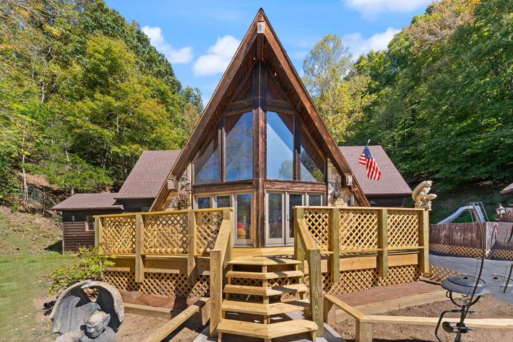 Rear exterior of A-frame home with steep roofline and wooded backdrop