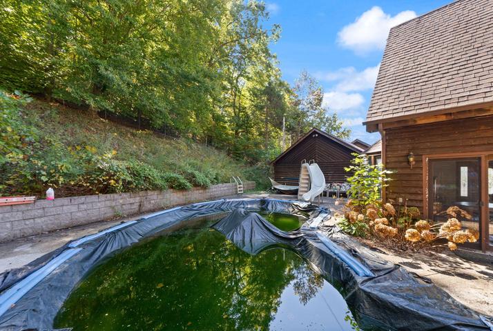 In-ground diving pool with diving board surrounded by patio and trees