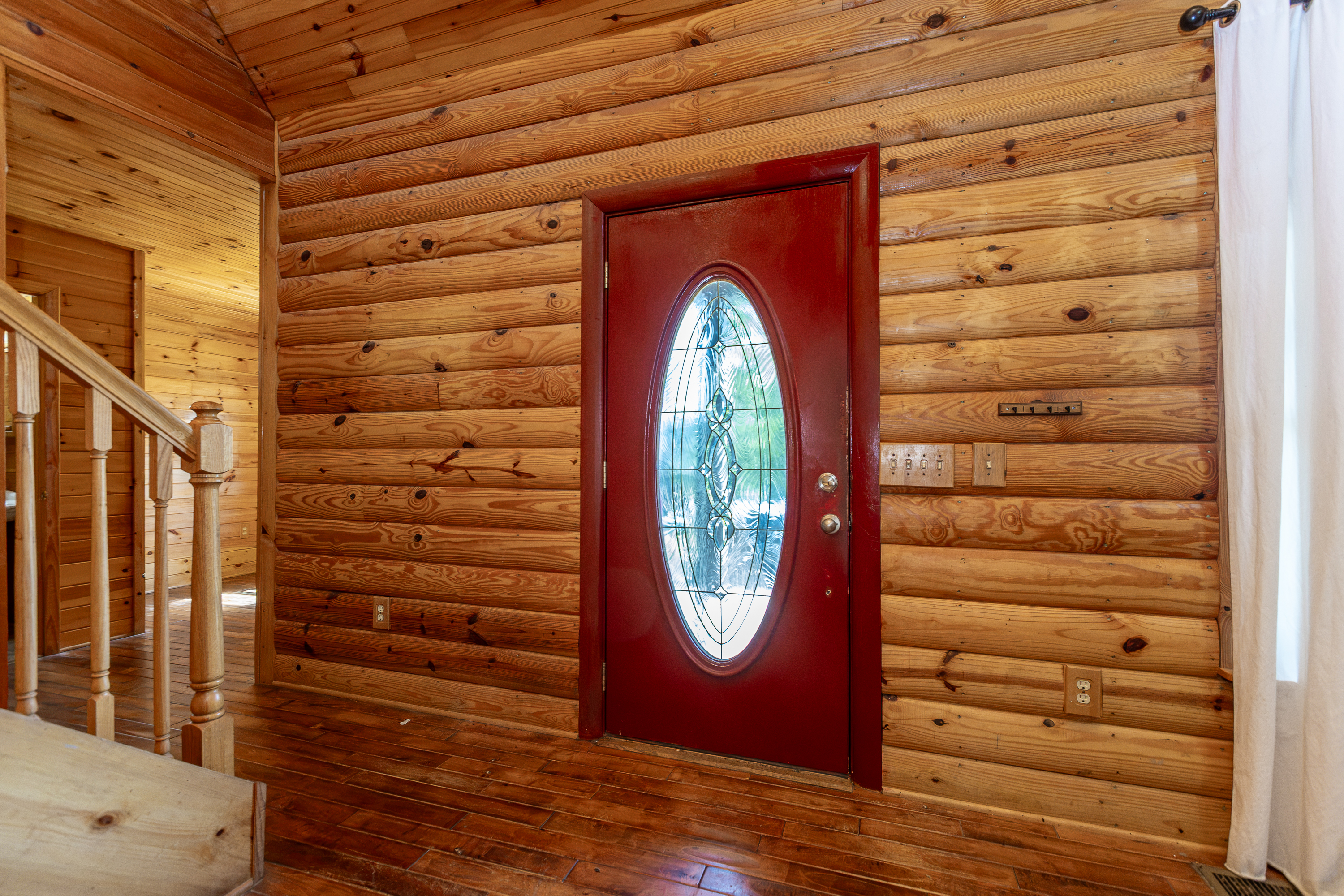 Entry foyer with red door, log walls, and staircase