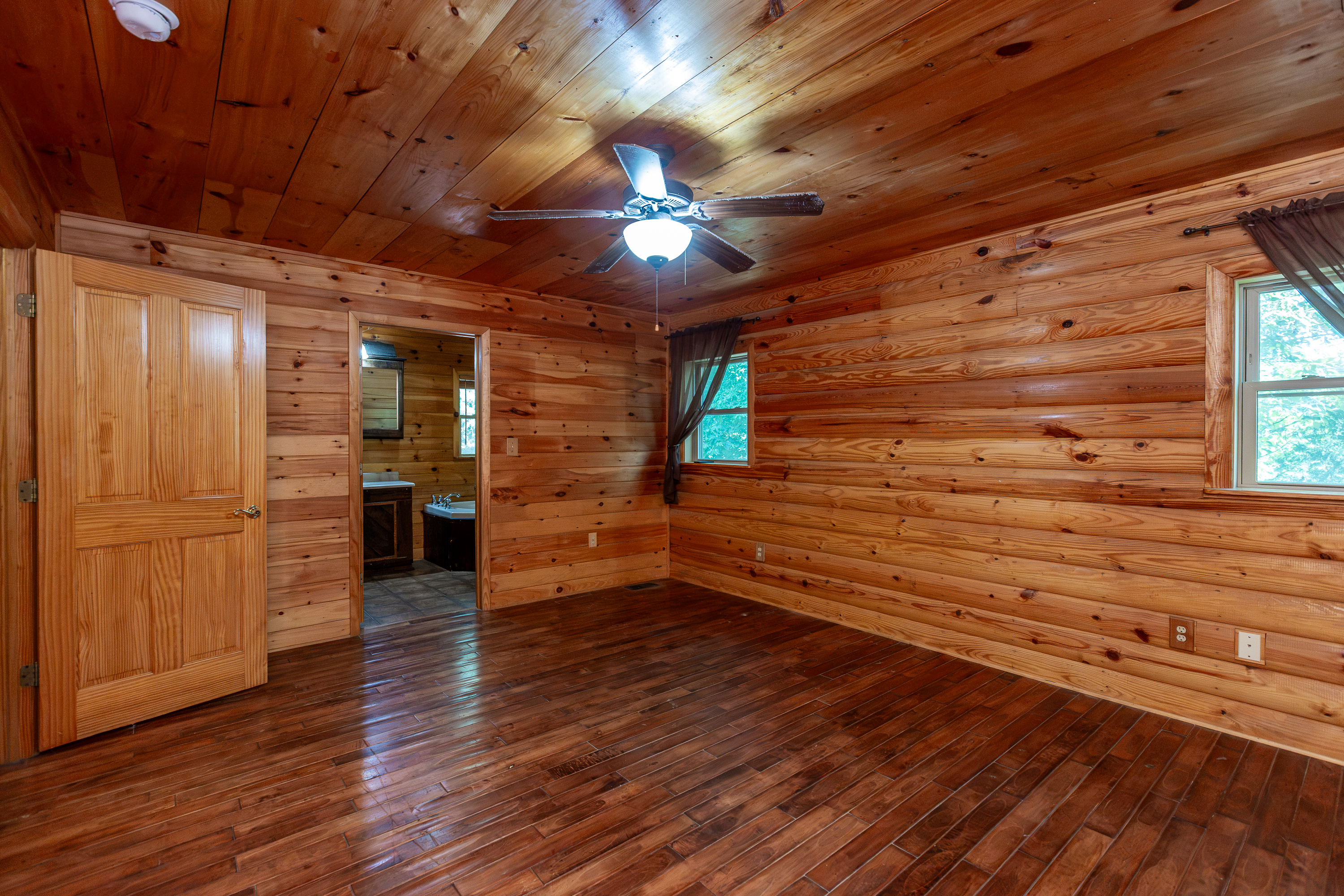 Primary bedroom with log walls, ceiling fan, and en-suite bath