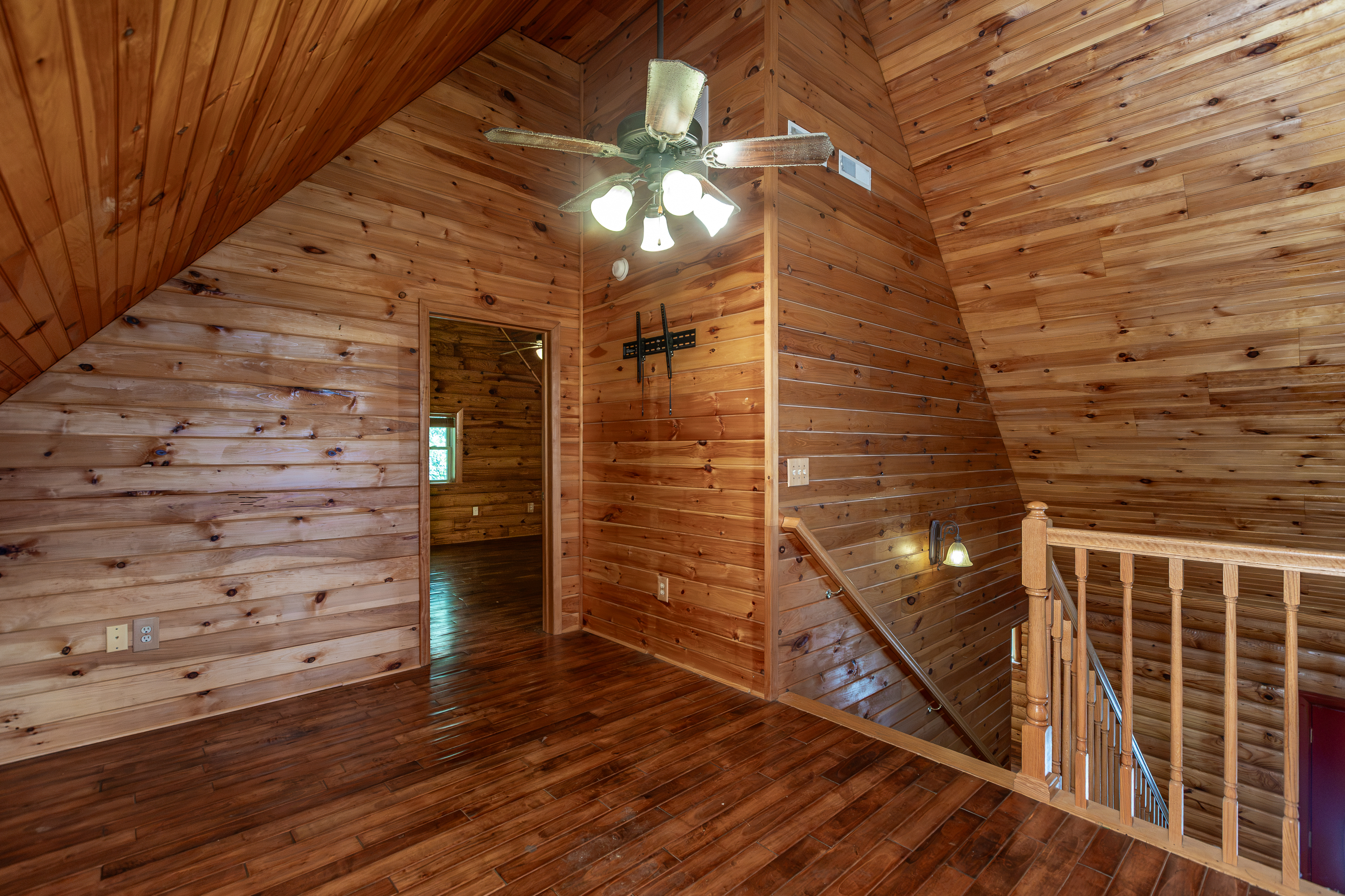 Loft area with vaulted log ceiling, ceiling fan, and staircase railing