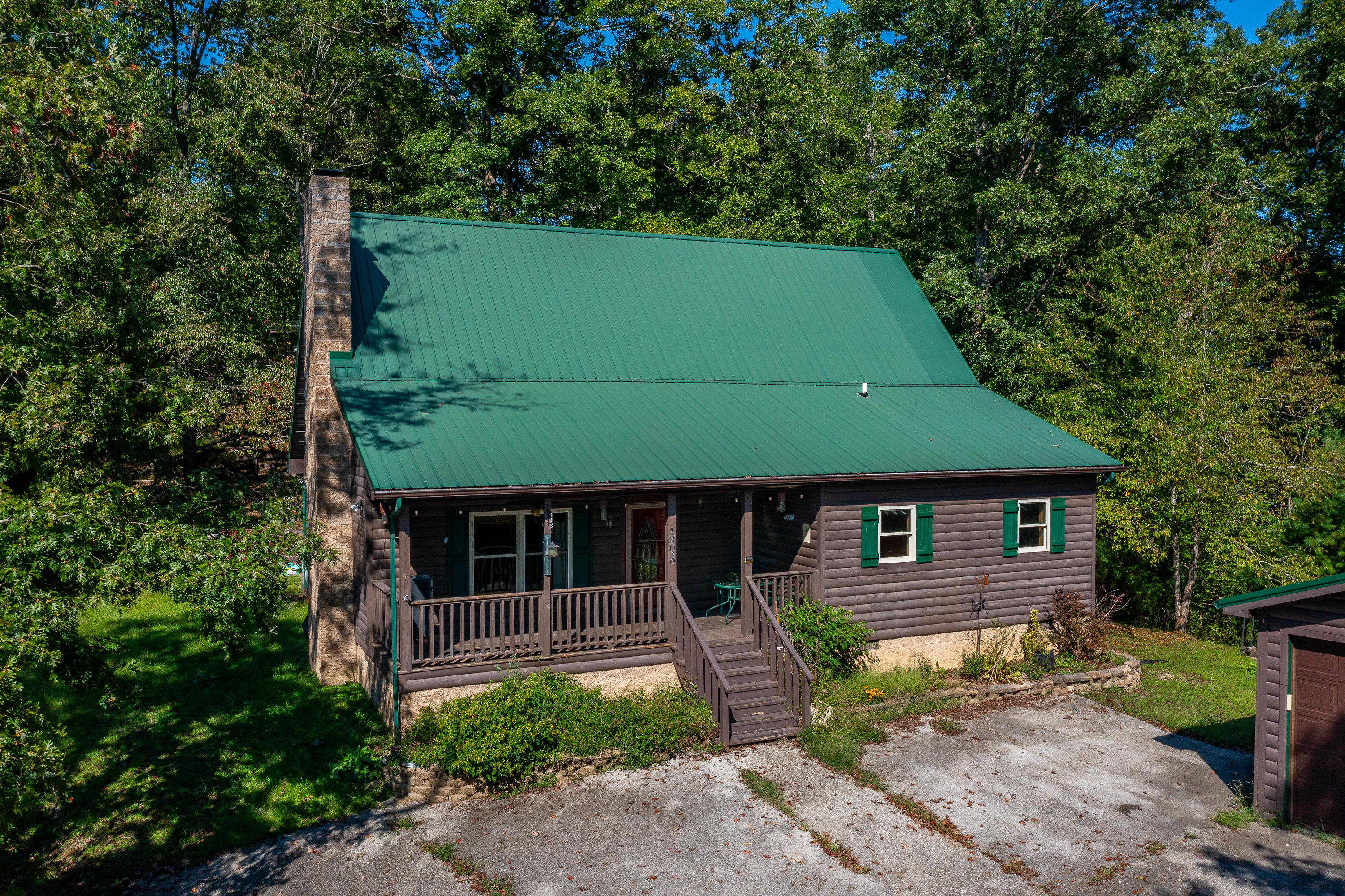 Aerial view of log home with green metal roof on hilltop surrounded by trees in Grassy Creek, Kentucky